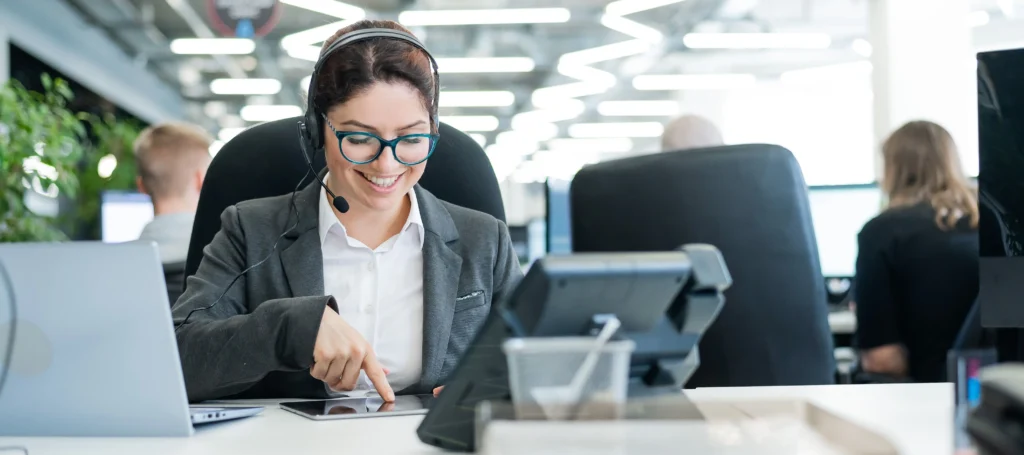 Smiling call center agent using a tablet and headset in a modern office environment, representing the future of BPO services